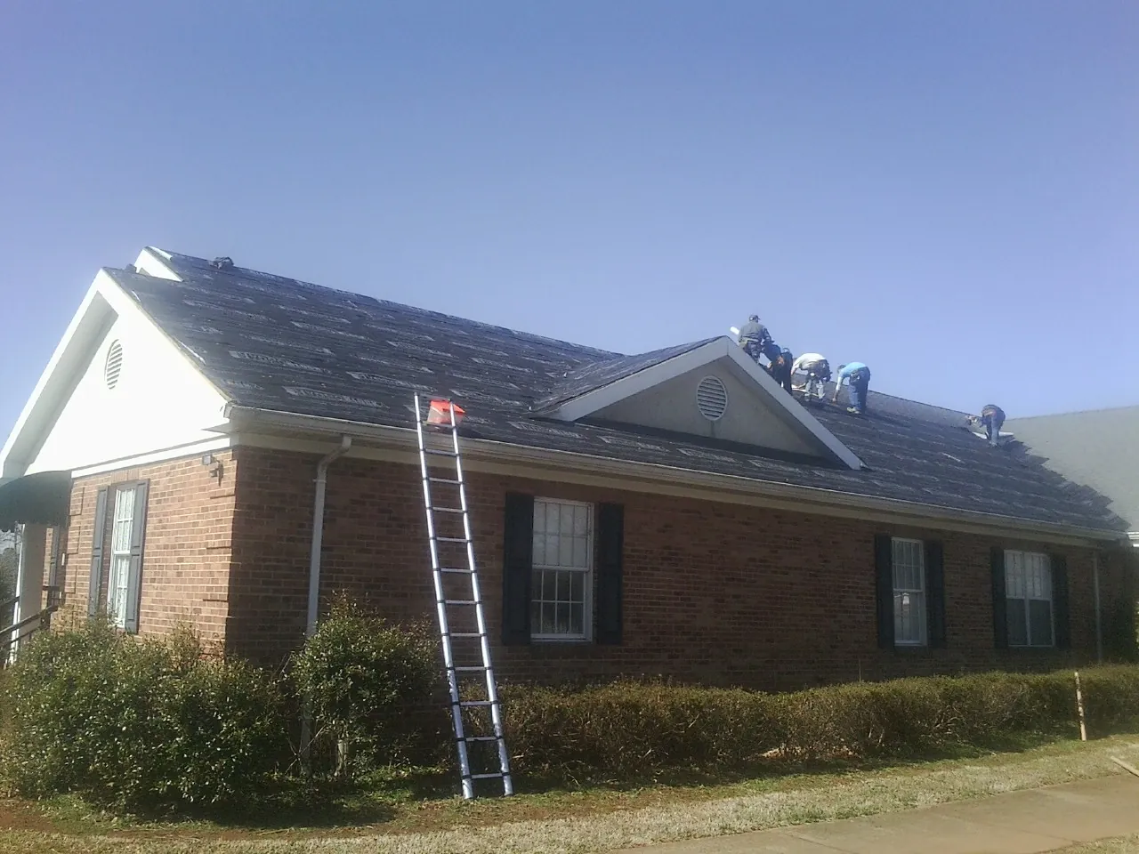 Crew tearing shingles off a brick ranch roof with a ladder set — Emergency Roof Repair work by our crew in Romeoville