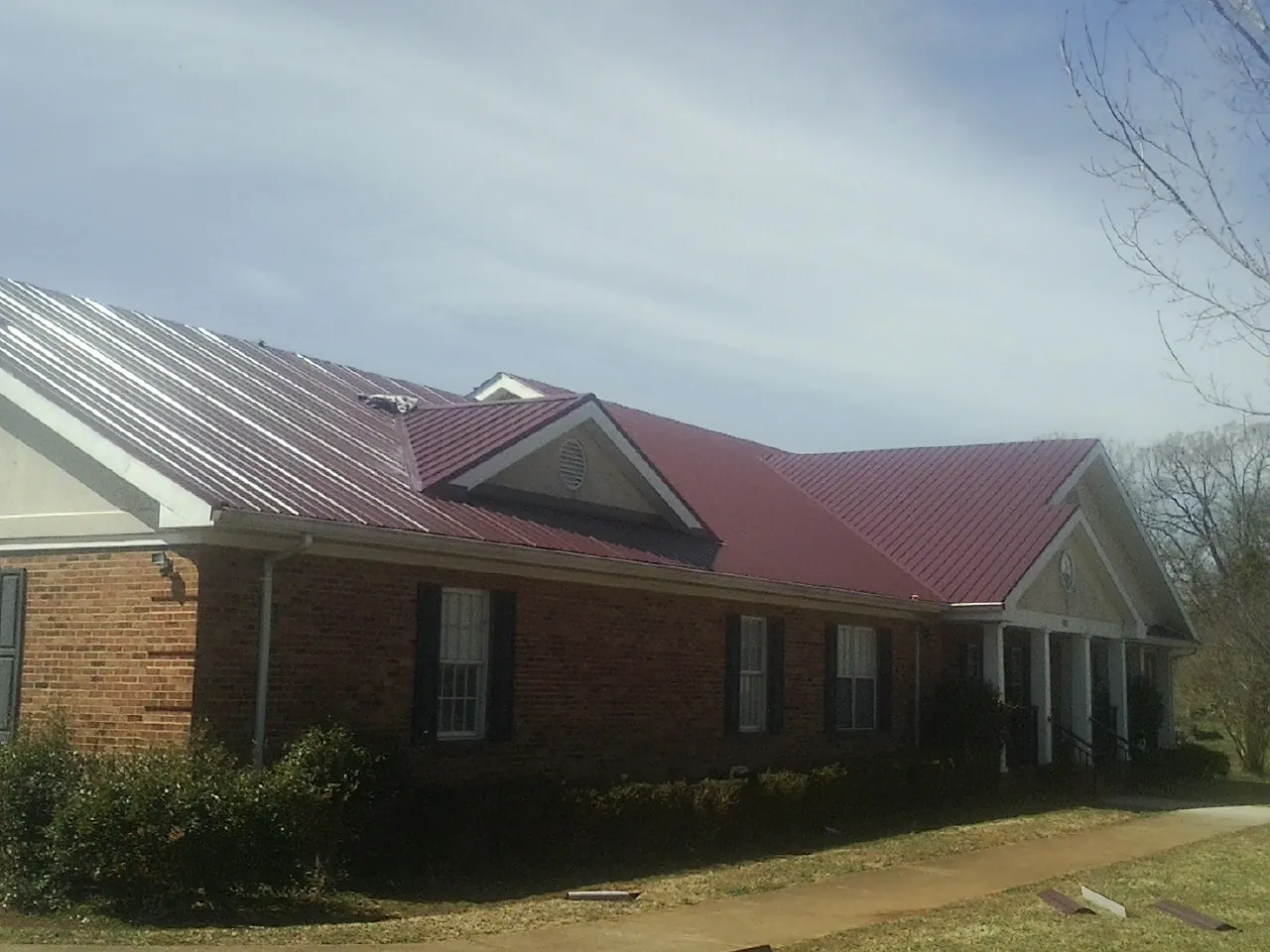 Red metal roof with gabled entries on a long brick building, from a Hail Damage Roof Repair job in Romeoville