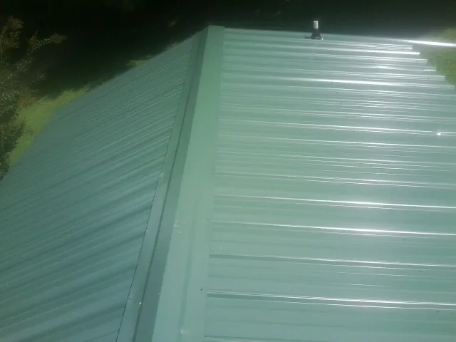 New green metal panels meeting at the ridge of a roof — Flat Roof Repair work by our crew in Romeoville