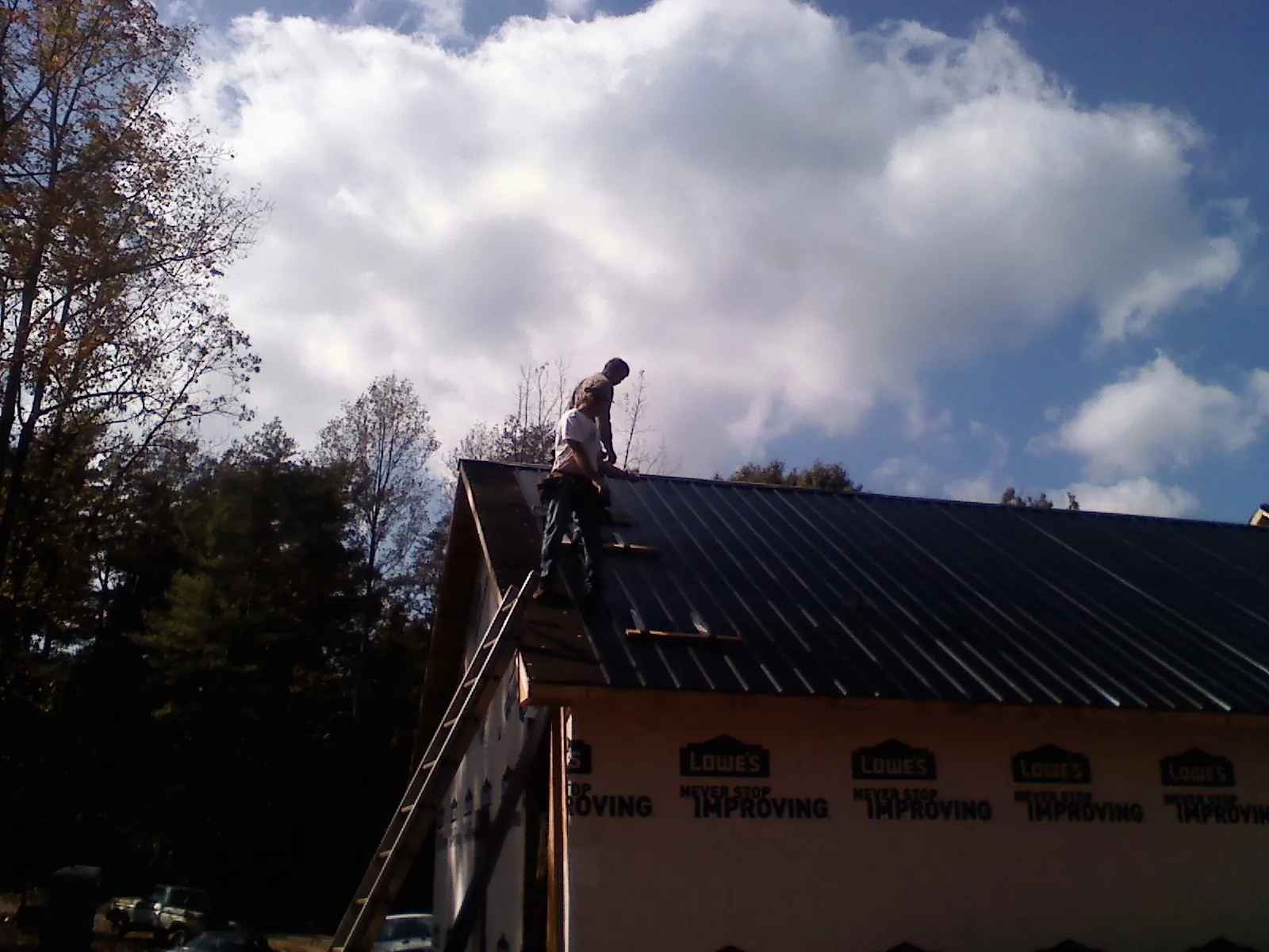 Roofer fastening dark metal panels high against a cloudy sky, from a Roof Inspection job in Romeoville