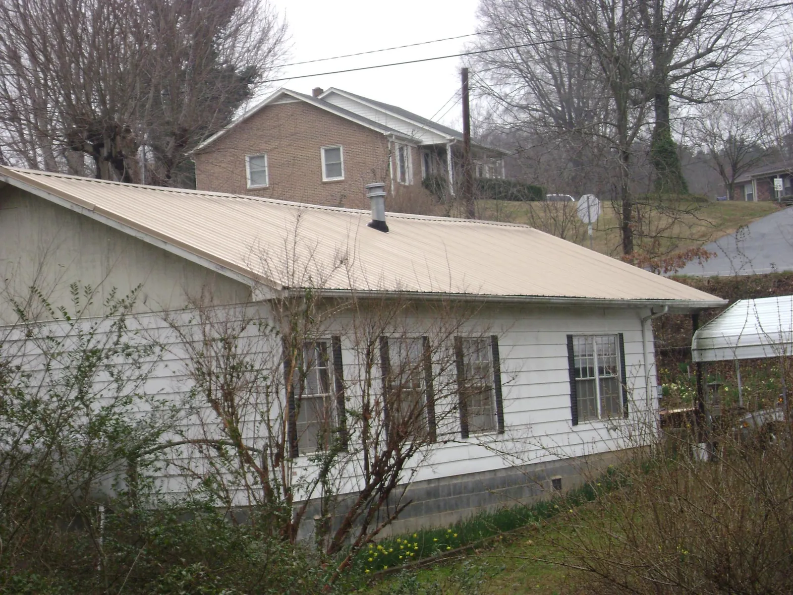 Tan metal roof on a white sided house set into a hillside — Commercial Roofing by Roofing Brothers in Romeoville